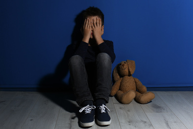 Abused little boy crying near blue wall. Domestic violence concept