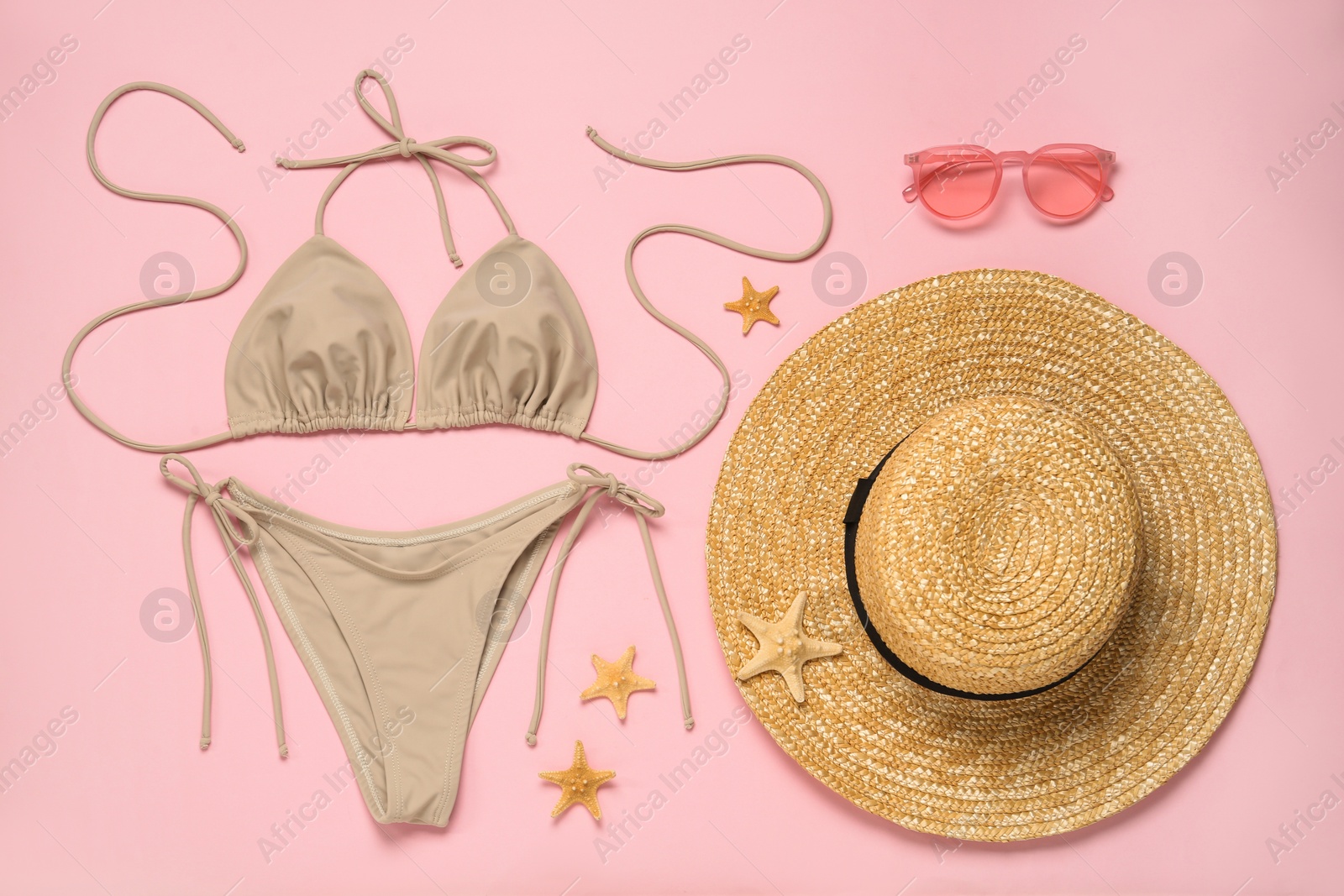 Photo of Stylish bikini, straw hat, sunglasses and starfishes on pink background, flat lay