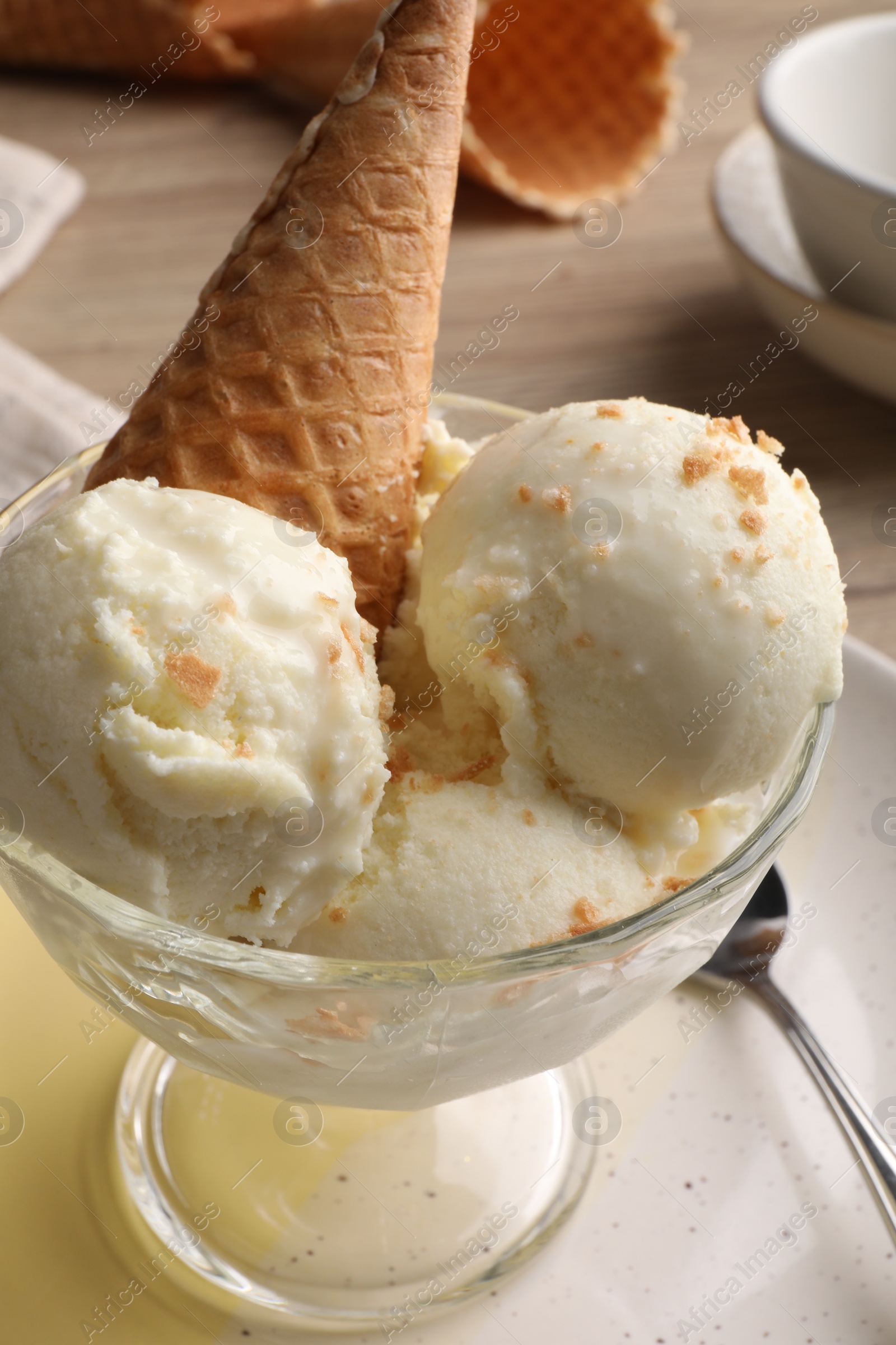 Photo of Delicious scoops of vanilla ice cream with wafer cone in glass dessert bowl on table, closeup