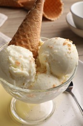 Photo of Delicious scoopsvanilla ice cream with wafer cone in glass dessert bowl on table, closeup