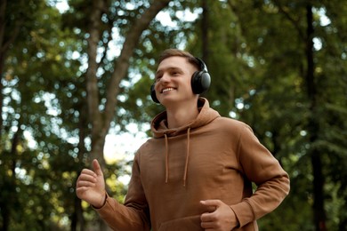 Photo of Smiling man in headphones running in park, low angle view