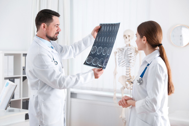 Photo of Professional orthopedist and his colleague examining X-ray picture in office