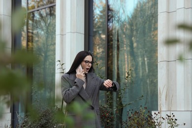 Photo of Emotional woman checking time while talking on smartphone outdoors. Being late concept