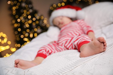 Baby in Christmas pajamas and Santa hat sleeping on bed indoors, focus on feet