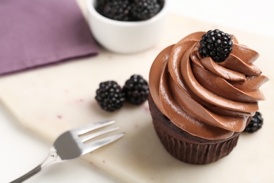 Photo of Delicious chocolate cupcake with cream and blackberries on white board, closeup