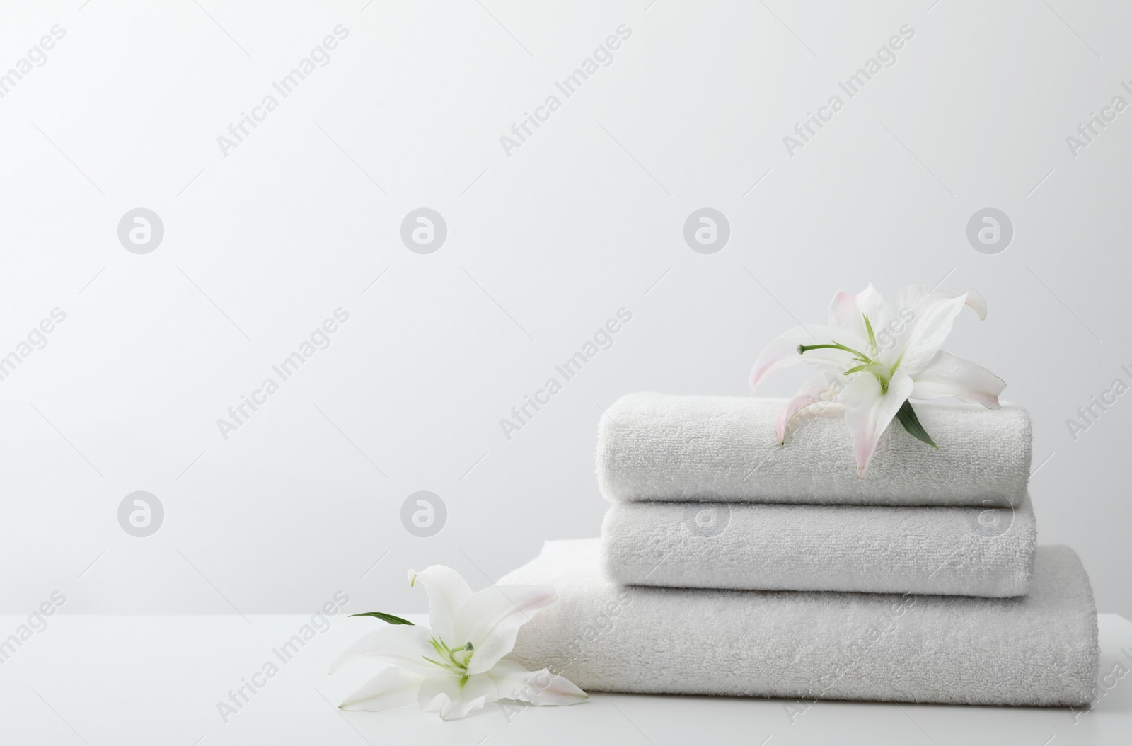 Photo of Stack of fresh towels with flowers on table against white background. Space for text