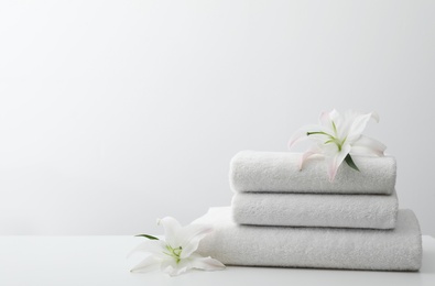 Stack of fresh towels with flowers on table against white background. Space for text