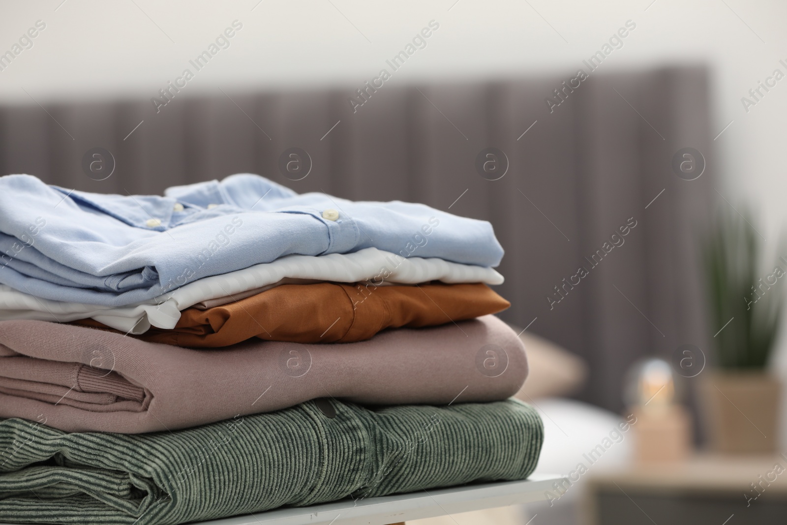 Photo of Stack of different folded clothes on table indoors, closeup. Space for text