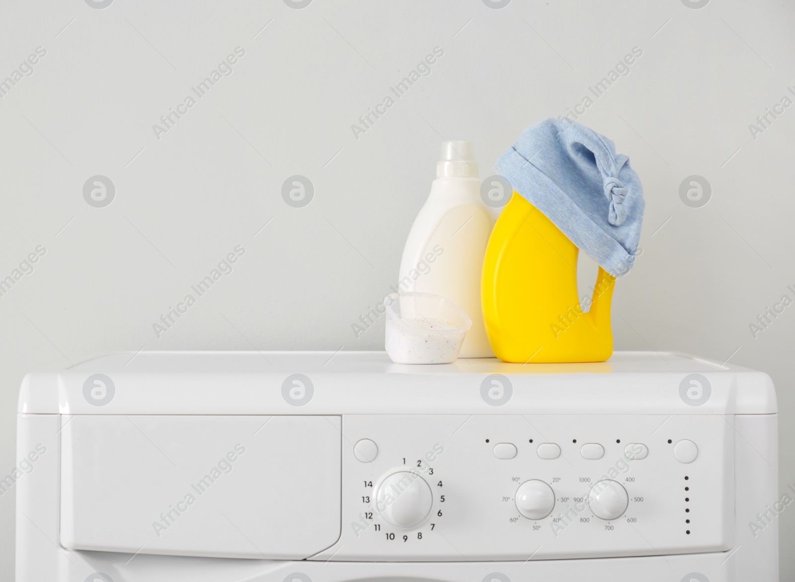 Photo of Bottles of detergent and children's hat on washing machine. Space for text