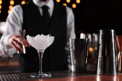 Bartender preparing fresh alcoholic cocktail in martini glass at bar counter, closeup