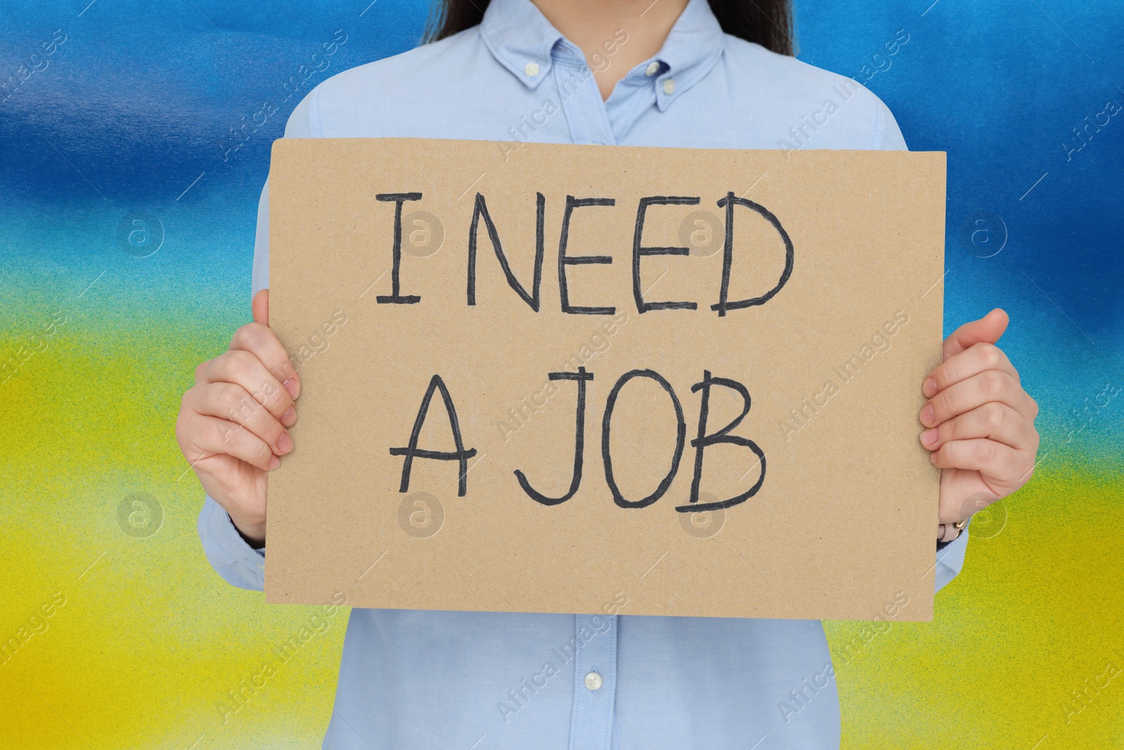 Image of Unemployed due to war. Woman holding cardboard sheet with phrase I Need A Job against colors of Ukrainian flag, closeup