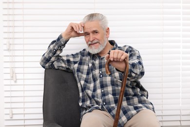 Photo of Senior man with walking cane sitting on armchair at home