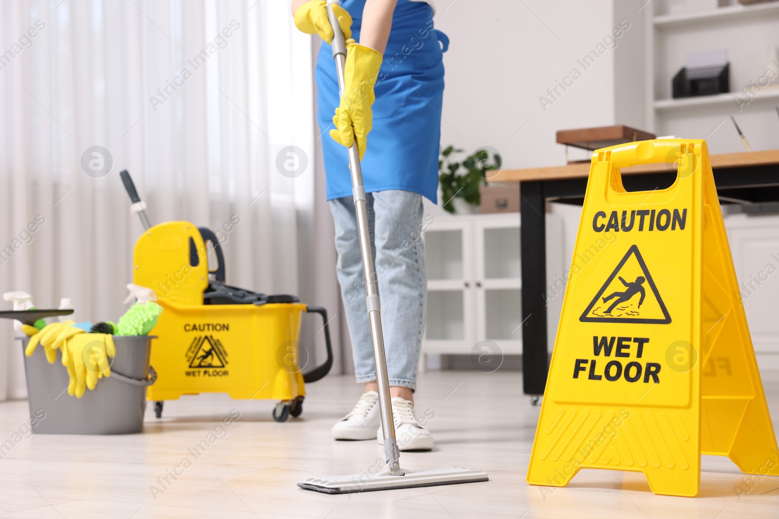 Photo of Cleaning service worker washing floor with mop, closeup. Bucket with supplies and wet floor sign in office