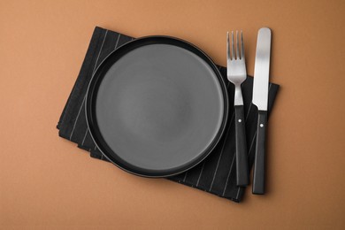 Clean plate with cutlery and napkin on light brown background, flat lay