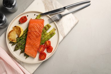 Photo of Tasty grilled salmon with asparagus, tomatoes, spices and lemon served on light grey table, top view. Space for text