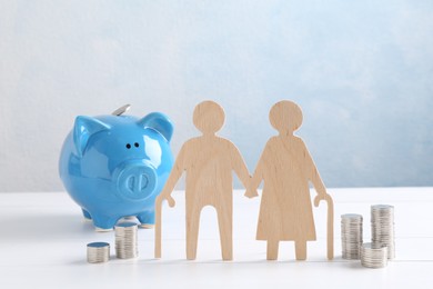 Pension savings. Figure of senior couple, stacked coins and piggy bank on white wooden table