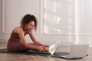 Photo of Beautiful African American woman stretching on yoga mat while watching online class indoors