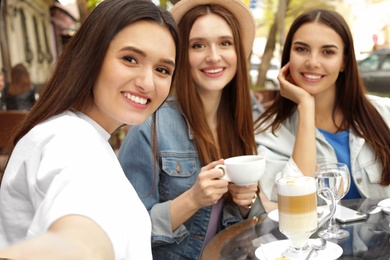 Photo of Happy beautiful girls taking selfie in cafe outdoors