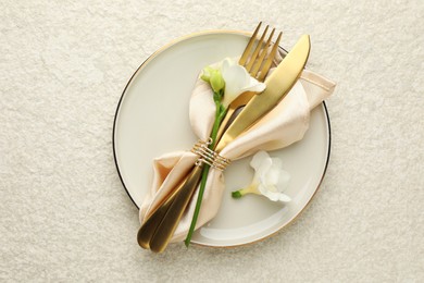 Photo of Stylish setting with cutlery, napkin, flowers and plate on light textured table, top view