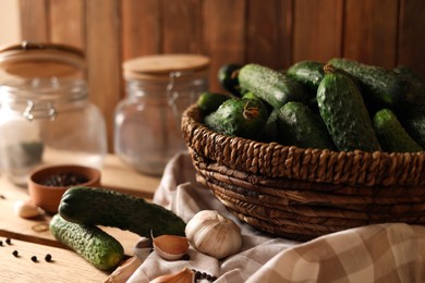Fresh cucumbers and other ingredients near jars prepared for canning on wooden table