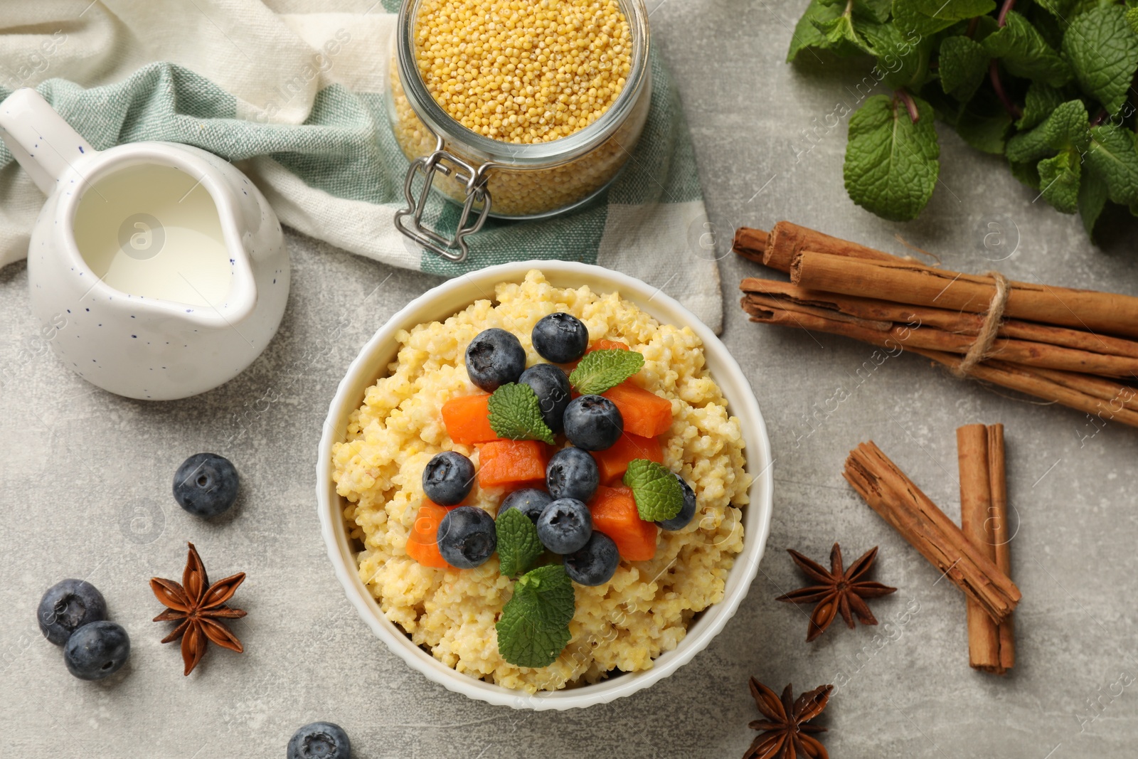 Photo of Tasty millet porridge with blueberries, pumpkin and mint in bowl on light grey table, flat lay