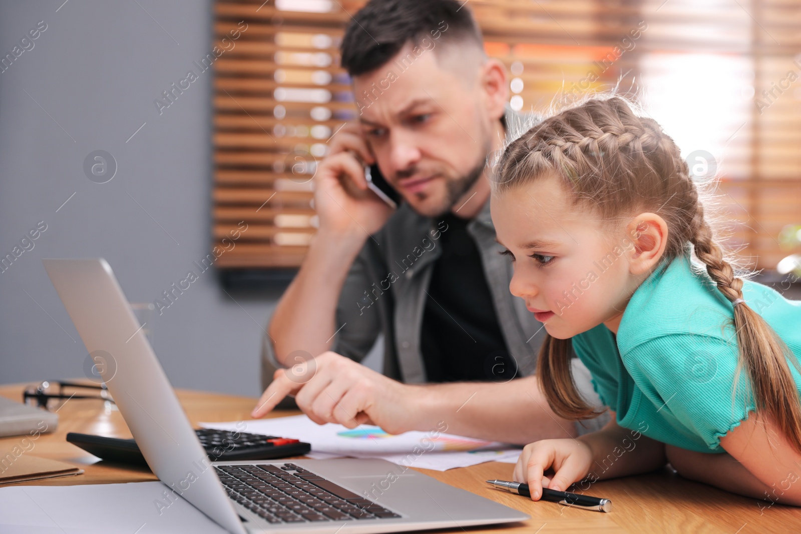 Photo of Little girl near laptop in father's office. Combining parenting and work