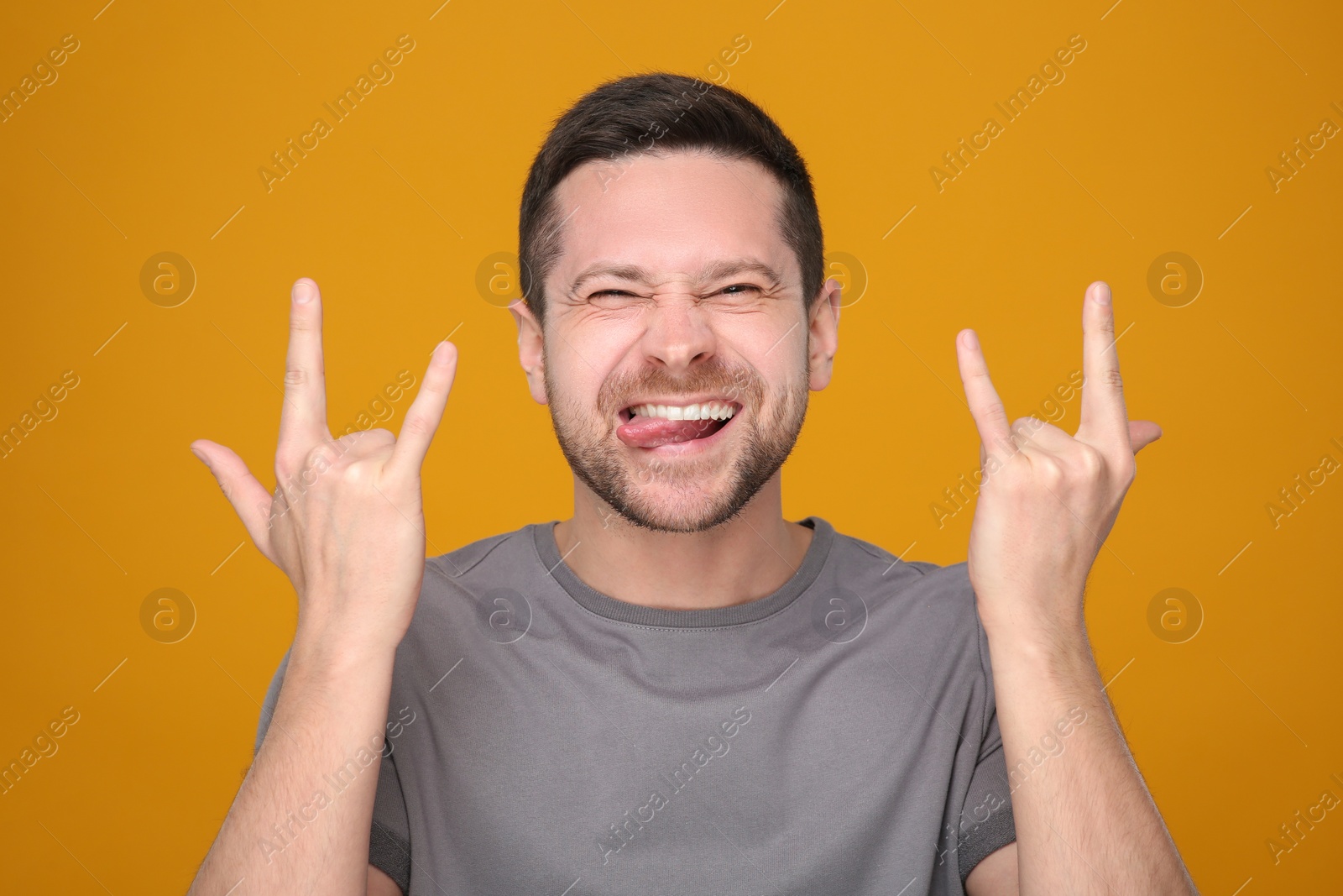 Photo of Happy man showing his tongue and rock gesture on orange background