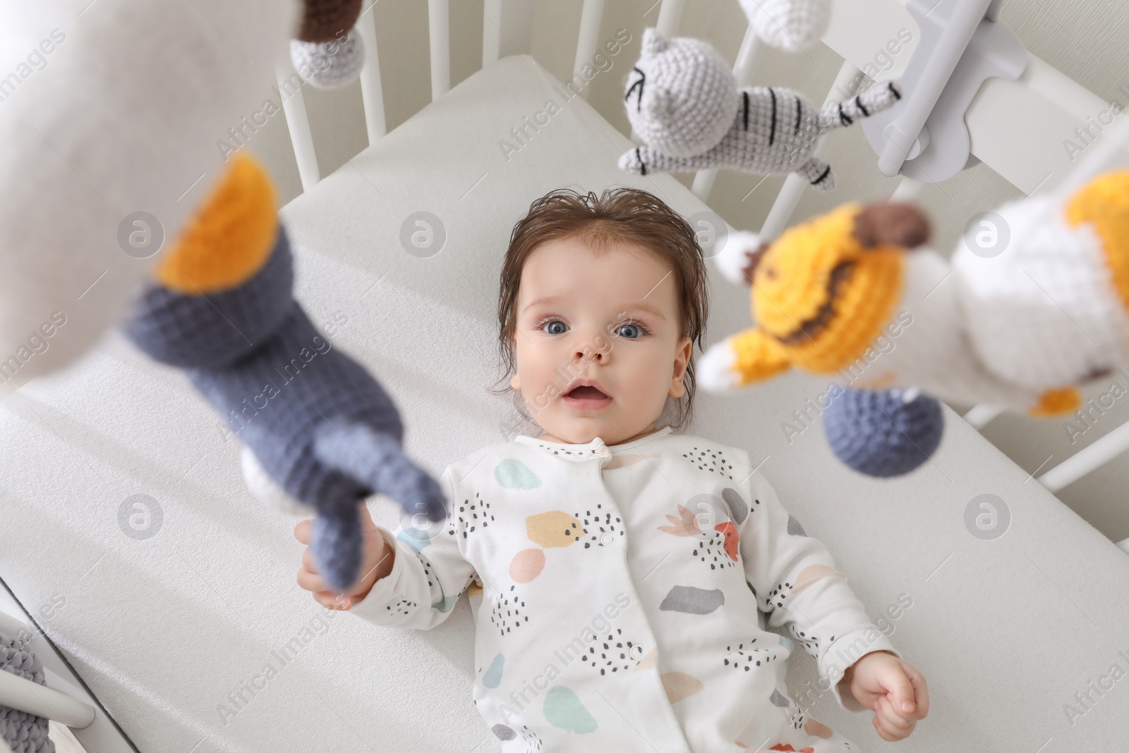 Photo of Cute little baby looking at hanging mobile in crib, above view