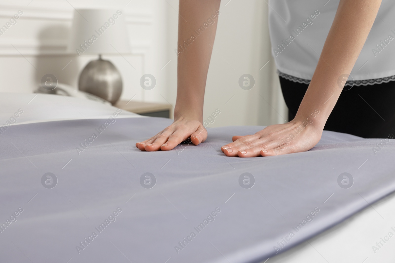 Photo of Young maid making bed in hotel room, closeup