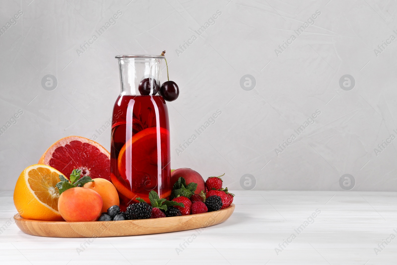 Photo of Delicious refreshing sangria, fruits and berries on white wooden table, space for text
