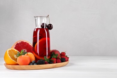 Photo of Delicious refreshing sangria, fruits and berries on white wooden table, space for text