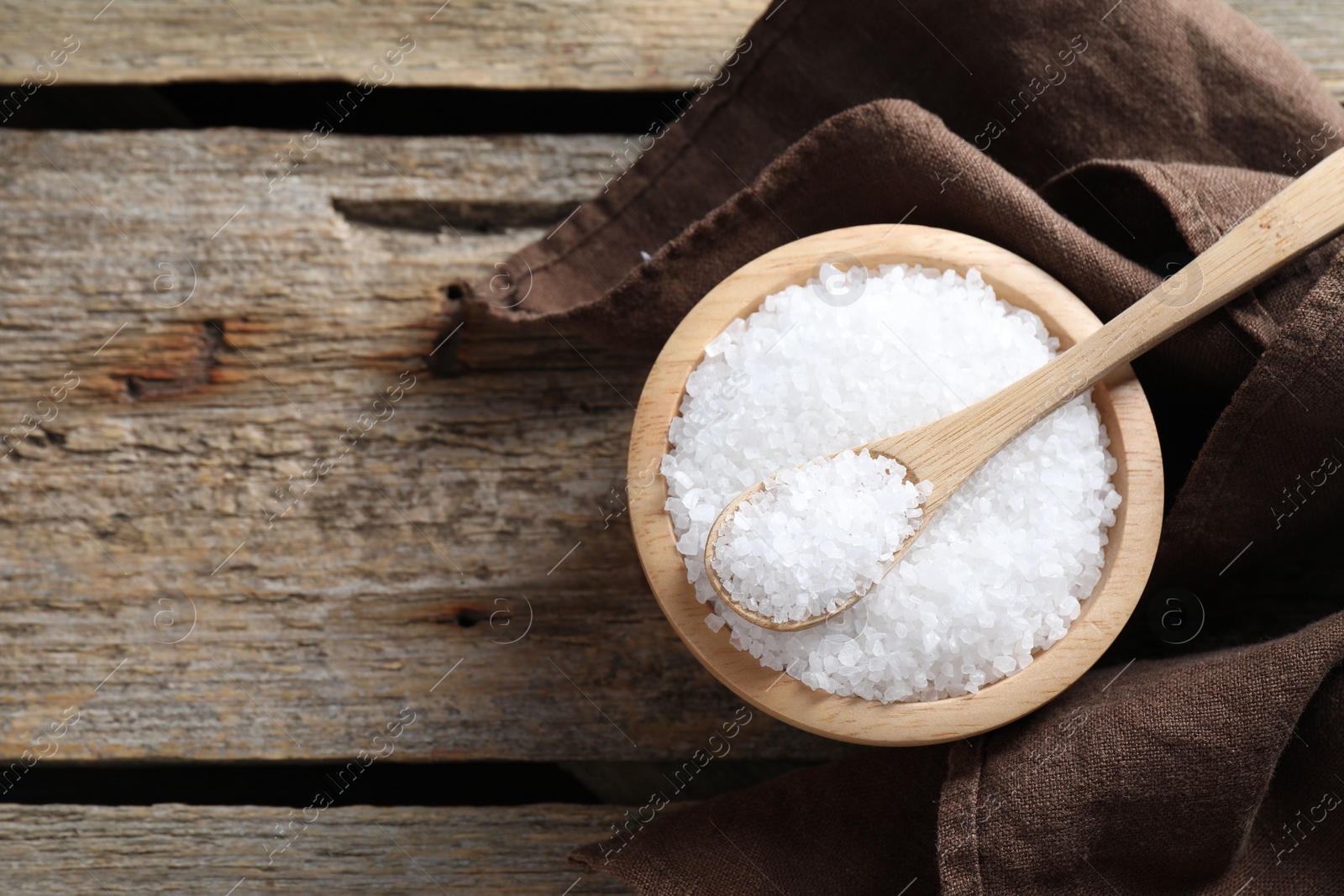 Photo of Organic salt in bowl and spoon on wooden table, top view. Space for text