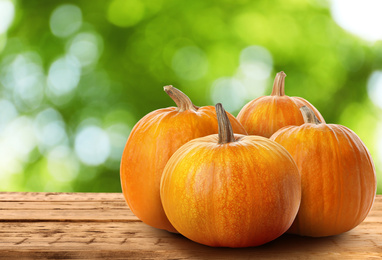 Image of Fresh pumpkins on wooden table against blurred greenery
