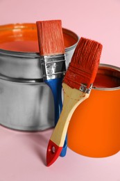 Photo of Bucket of orange paint, can and brushes on pink background, closeup