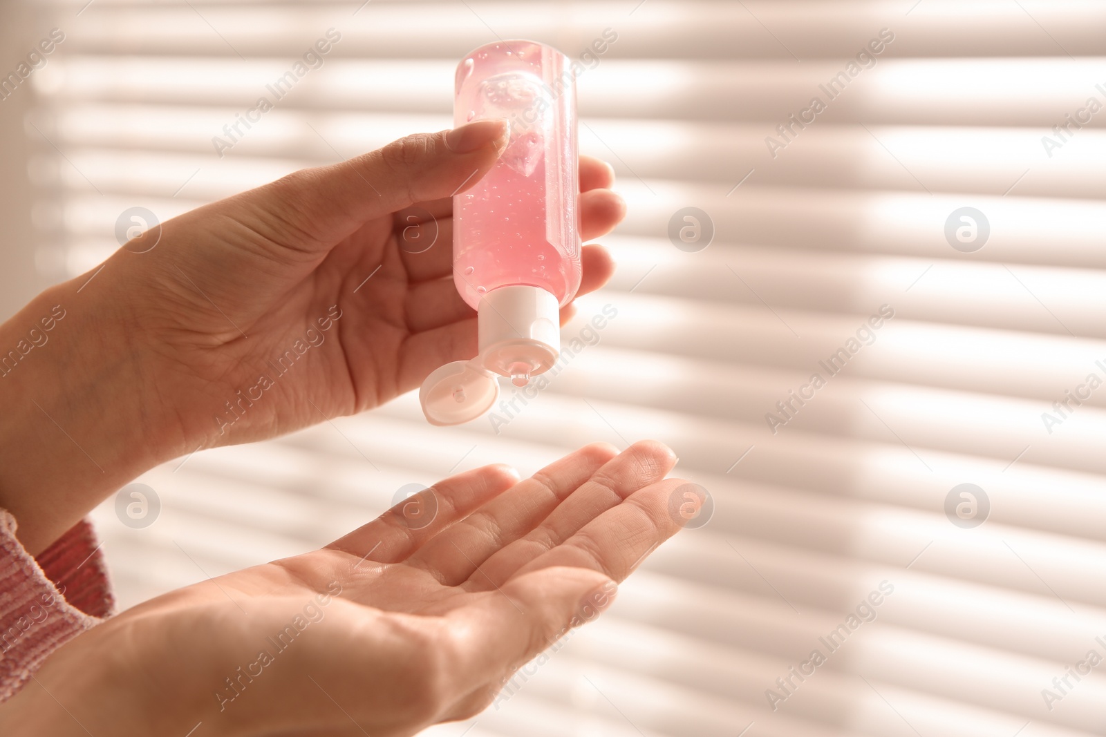 Photo of Woman applying antiseptic gel near window indoors, closeup