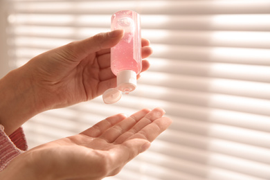 Photo of Woman applying antiseptic gel near window indoors, closeup