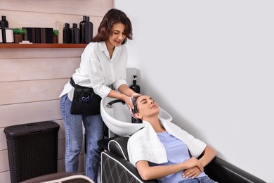 Photo of Professional hairdresser washing woman's hair in beauty salon