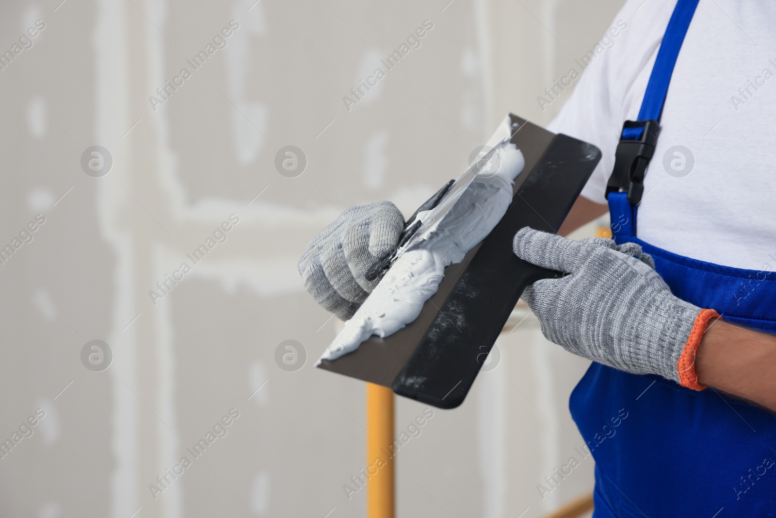 Photo of Worker with putty knives and plaster near wall, closeup. Space for text