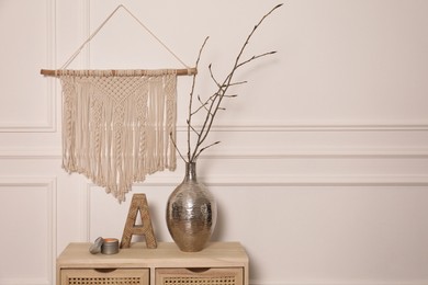 Photo of Tree twigs in metal vase and decor on wooden table near white wall. Space for text