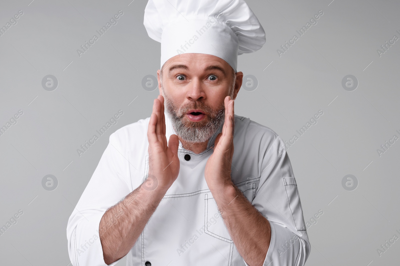 Photo of Surprised chef in uniform on grey background