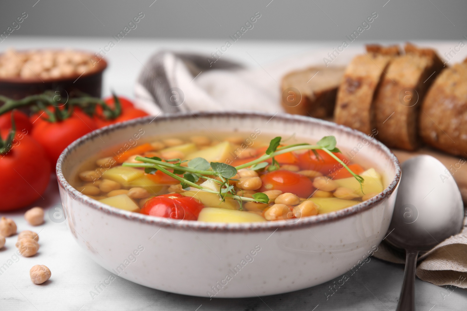 Photo of Tasty chickpea soup in bowl and ingredients served on white table, closeup