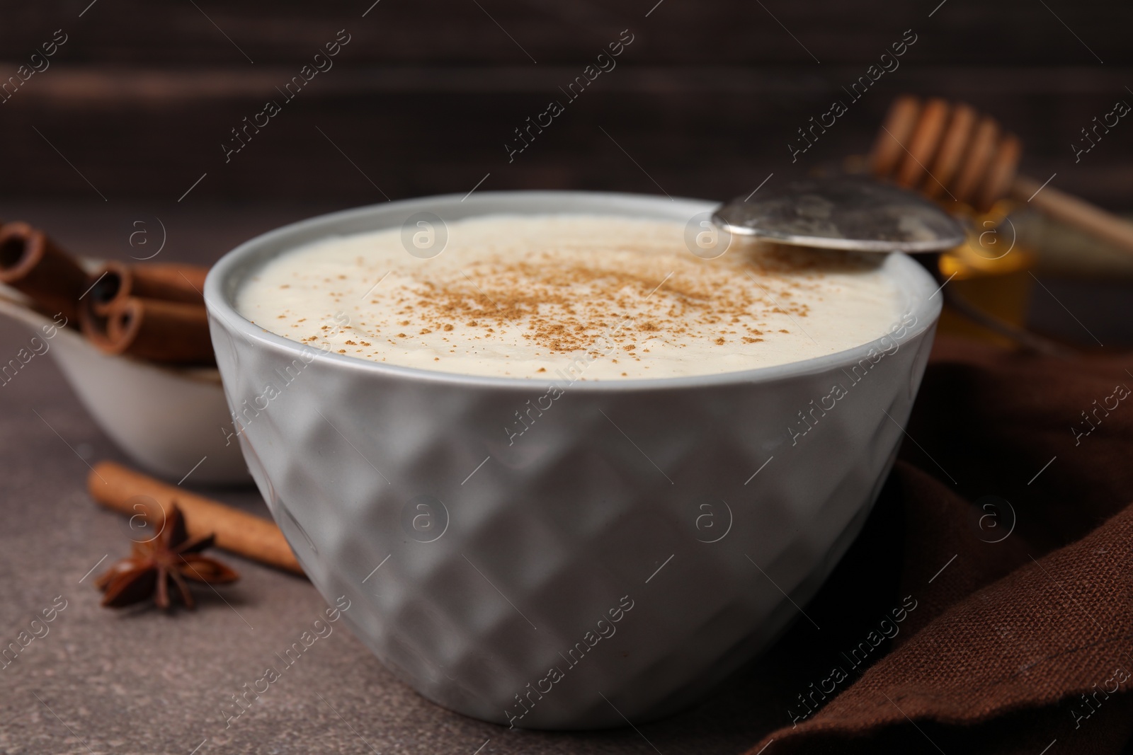 Photo of Delicious semolina pudding with cinnamon in bowl and spoon on brown table, closeup