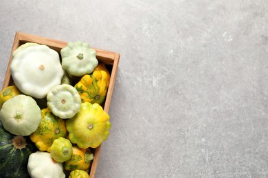 Fresh ripe pattypan squashes in wooden crate on light grey table, top view. Space for text