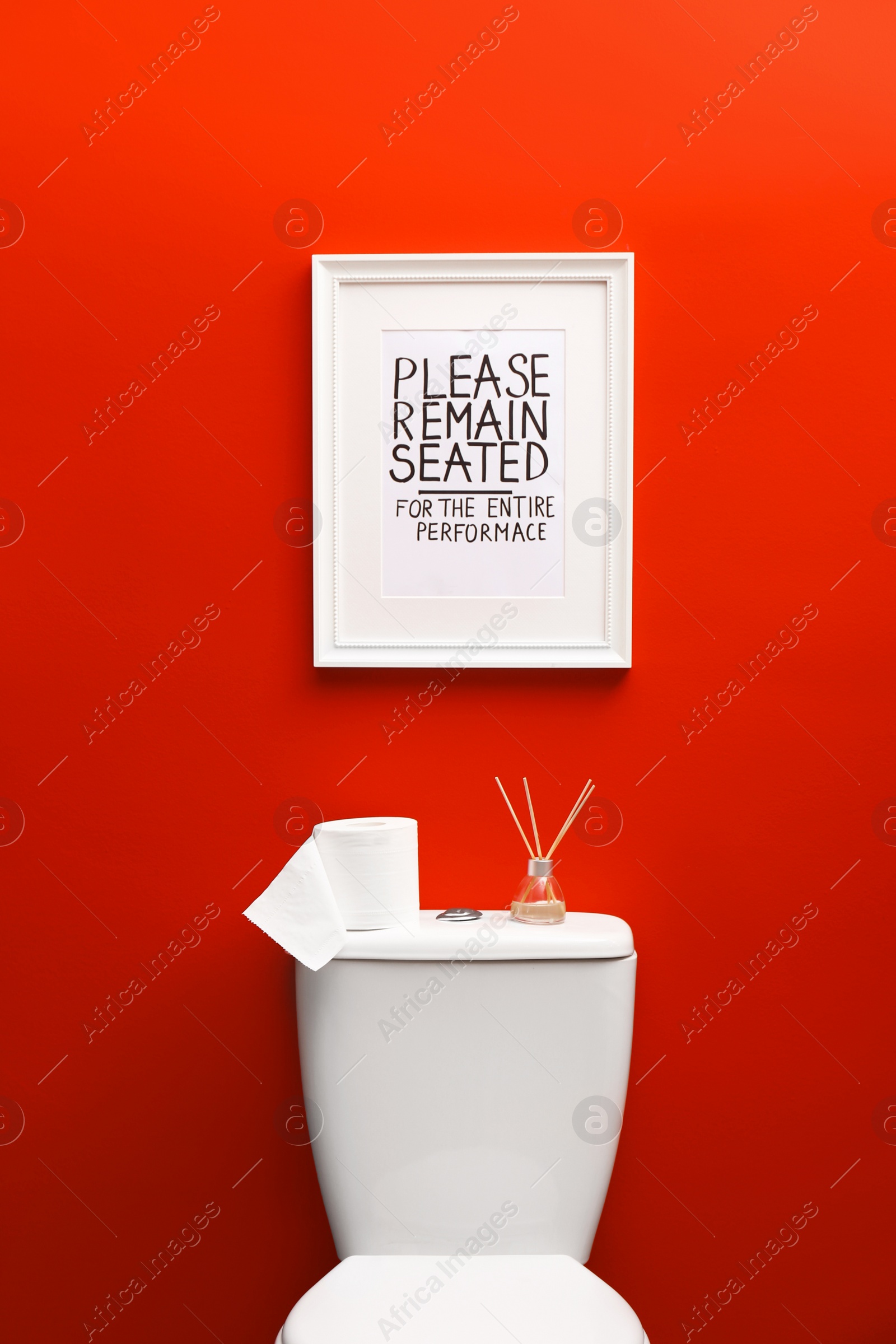 Photo of Toilet bowl and funny sign near red wall. Bathroom interior