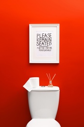 Photo of Toilet bowl and funny sign near red wall. Bathroom interior