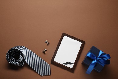 Photo of Empty photo frame, gift box and men accessories on brown background, flat lay with space for text. Father's day celebration