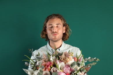 Young handsome man with beautiful flower bouquet on green background