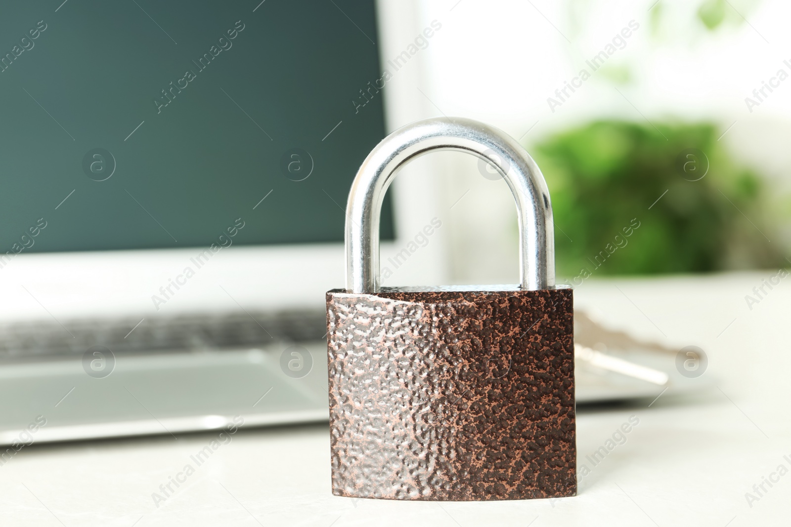 Photo of Metal lock and laptop on table, closeup. Protection from cyber attack