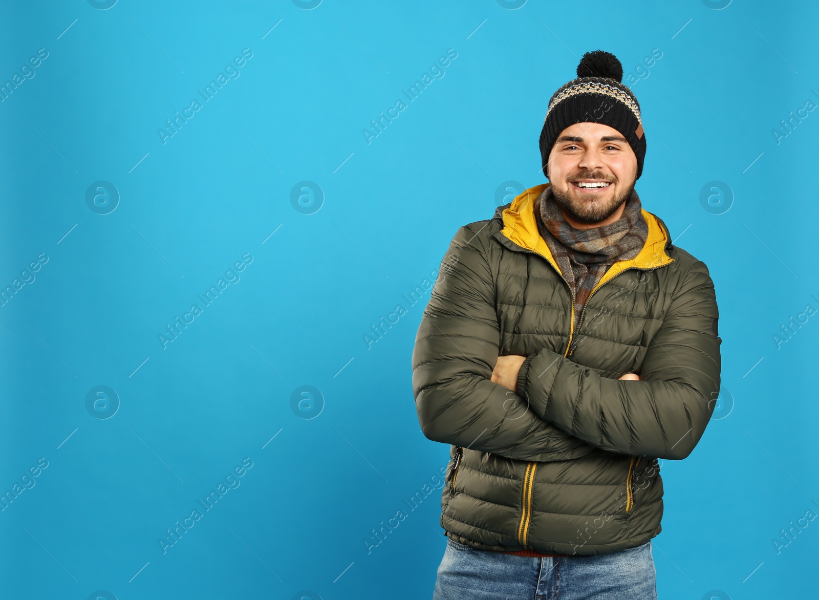 Photo of Happy young man in warm clothes on blue background, space for text. Winter vacation