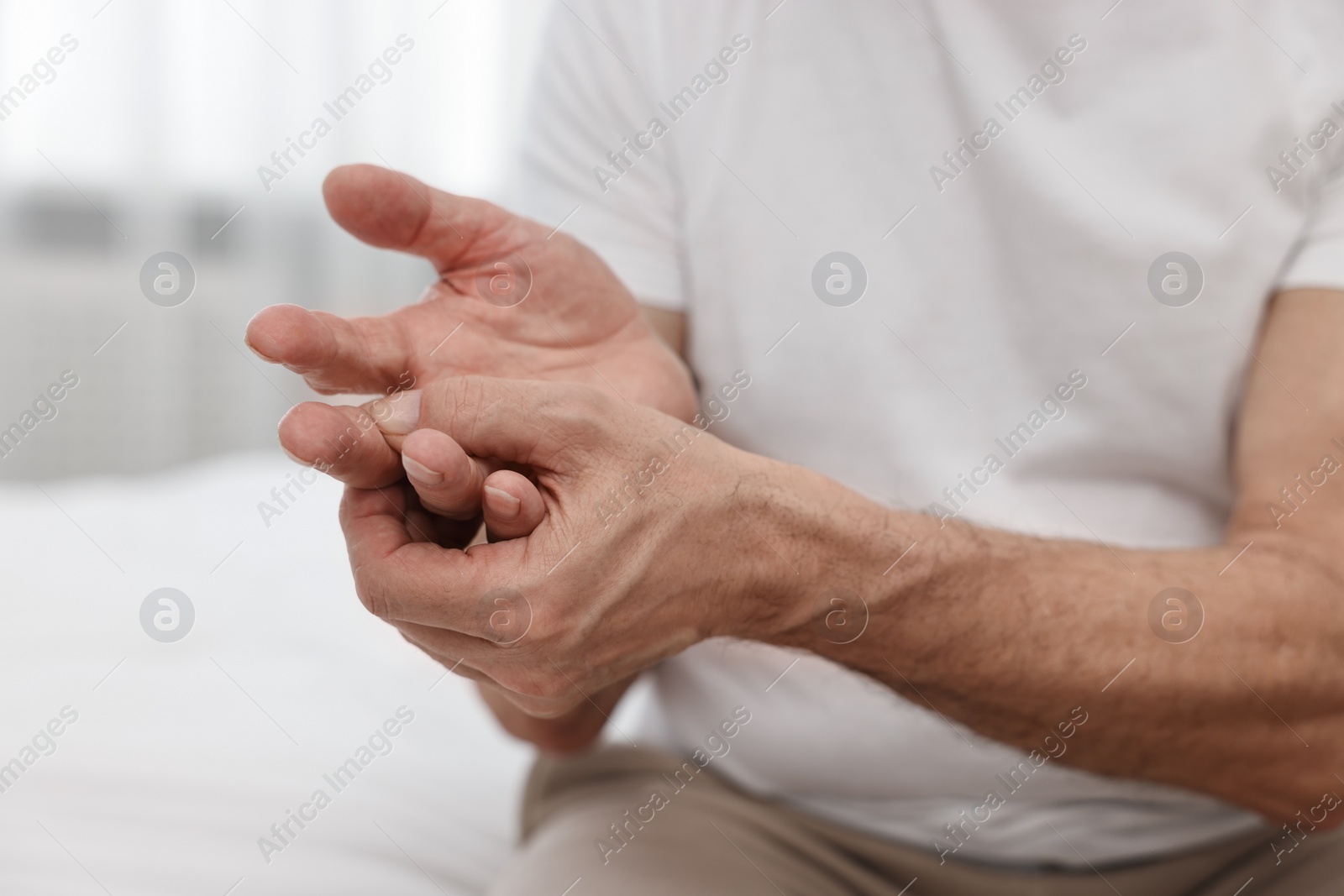 Photo of Arthritis symptoms. Man suffering from pain in hand on bed at home, closeup